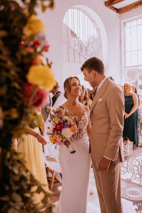 Braut und Bräutigam in eleganter Hochzeitsatmosphäre, umgeben von bunten Blumen.