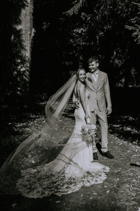 Braut und Bräutigam stehen umgeben von Natur in romantischer Schwarz-Weiß-Ästhetik.